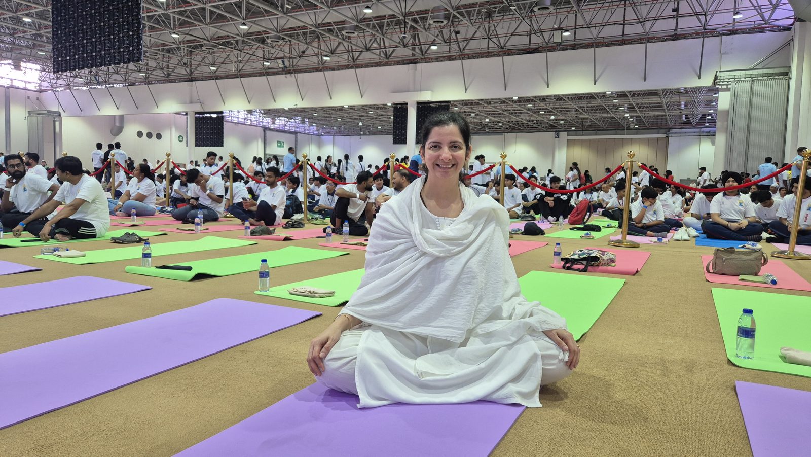Persis seated in white among hundreds of practitioners on coloured mats in a large hall