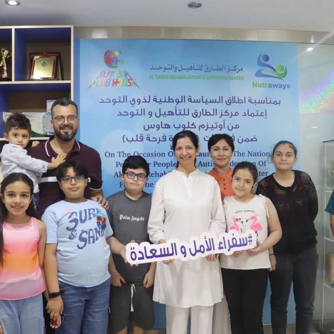 Persis with children, parents and staff in front of a banner marking the launch of the National Policy for People with Autism