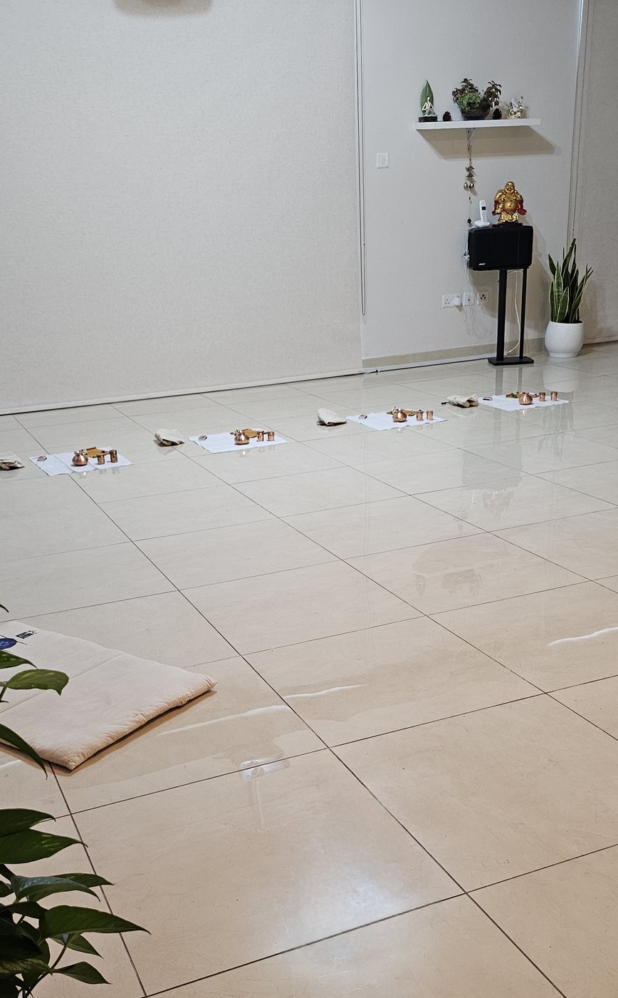 The studio floor before a class, with a row of cloths each holding a Bhuta Shuddhi kit and the teacher&rsquo;s seat at the front